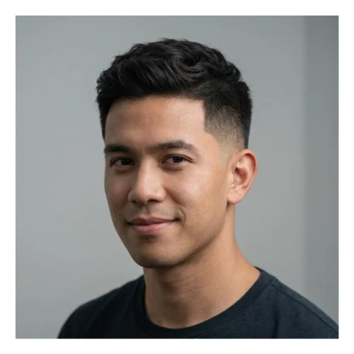 A young man with short hair styled in a low taper fade with a natural look, featuring smoothly tapered sides that blend into a slightly longer top, allowing the hair’s natural texture and movement to show for a relaxed, effortless style.